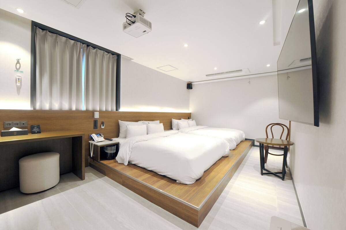 Una habitación de hotel moderna con una cama grande, un escritorio con teléfono, una silla y un televisor fijado a la pared.
