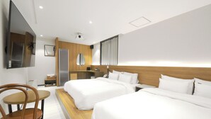 Habitación de hotel con dos camas, cabecero de madera, una mesita con silla, televisor montado en la pared y un espejo.