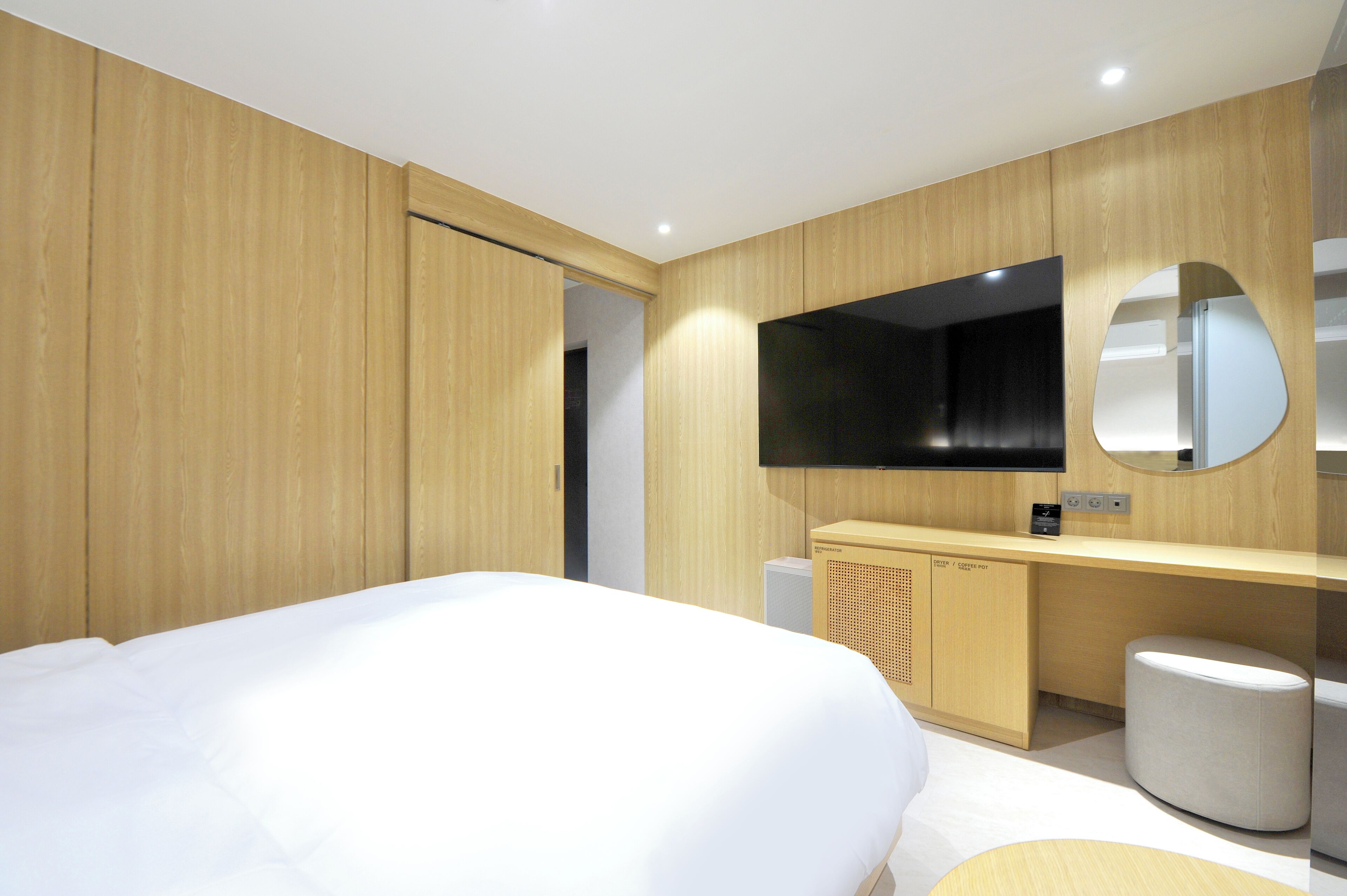 A modern hotel room with a large bed, wooden panel walls, a built-in TV, and a small seating area.