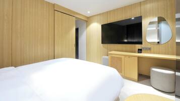 A modern hotel room with a large bed, wooden panel walls, a built-in TV, and a small seating area.