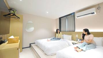 A hotel room with two beds, a desk, a basket, and an air conditioning unit.