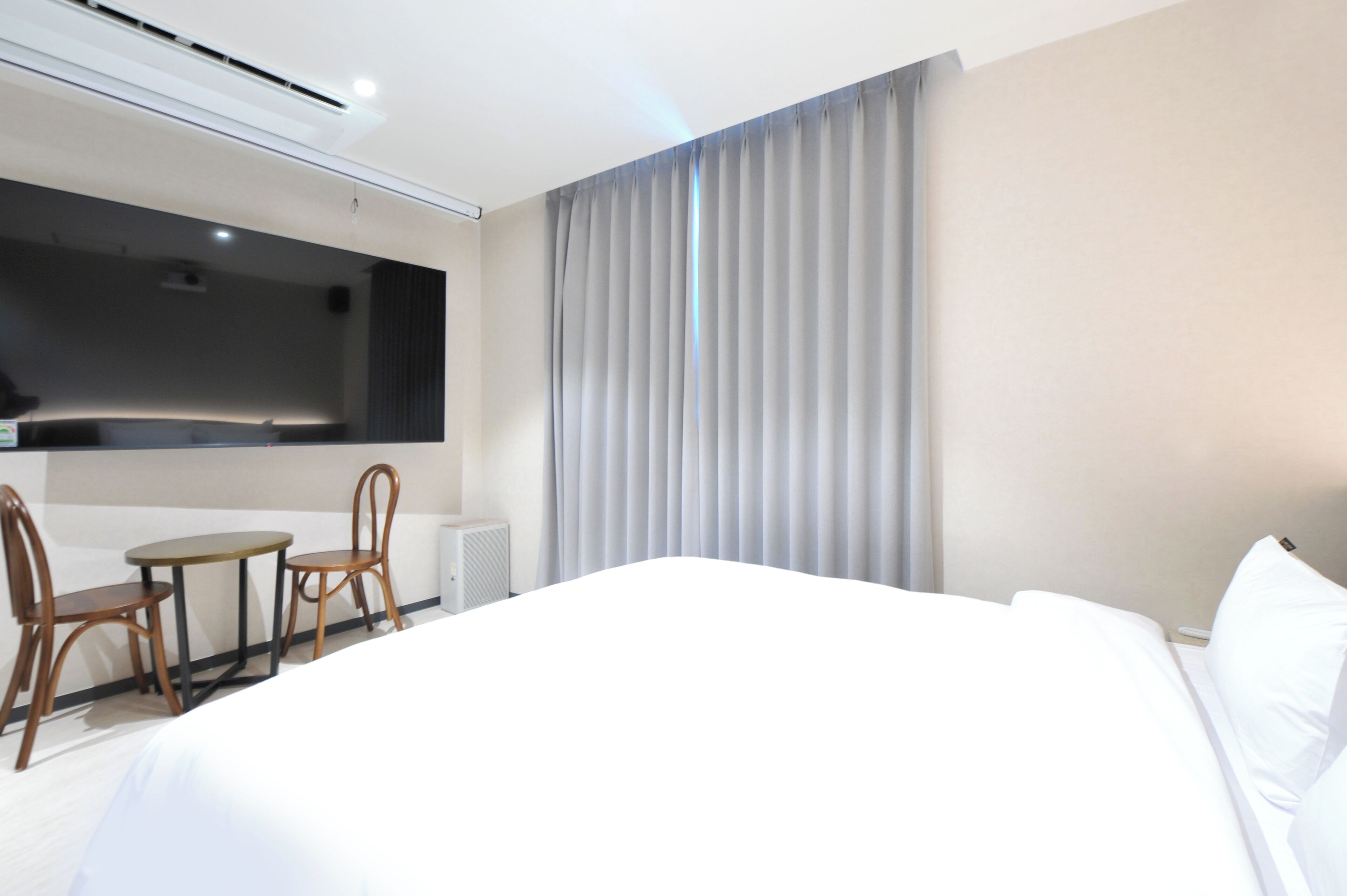 Habitación de hotel con una cama grande, un escritorio con dos sillas, un televisor de pantalla plana montado en la pared y un ventanal con cortinas.