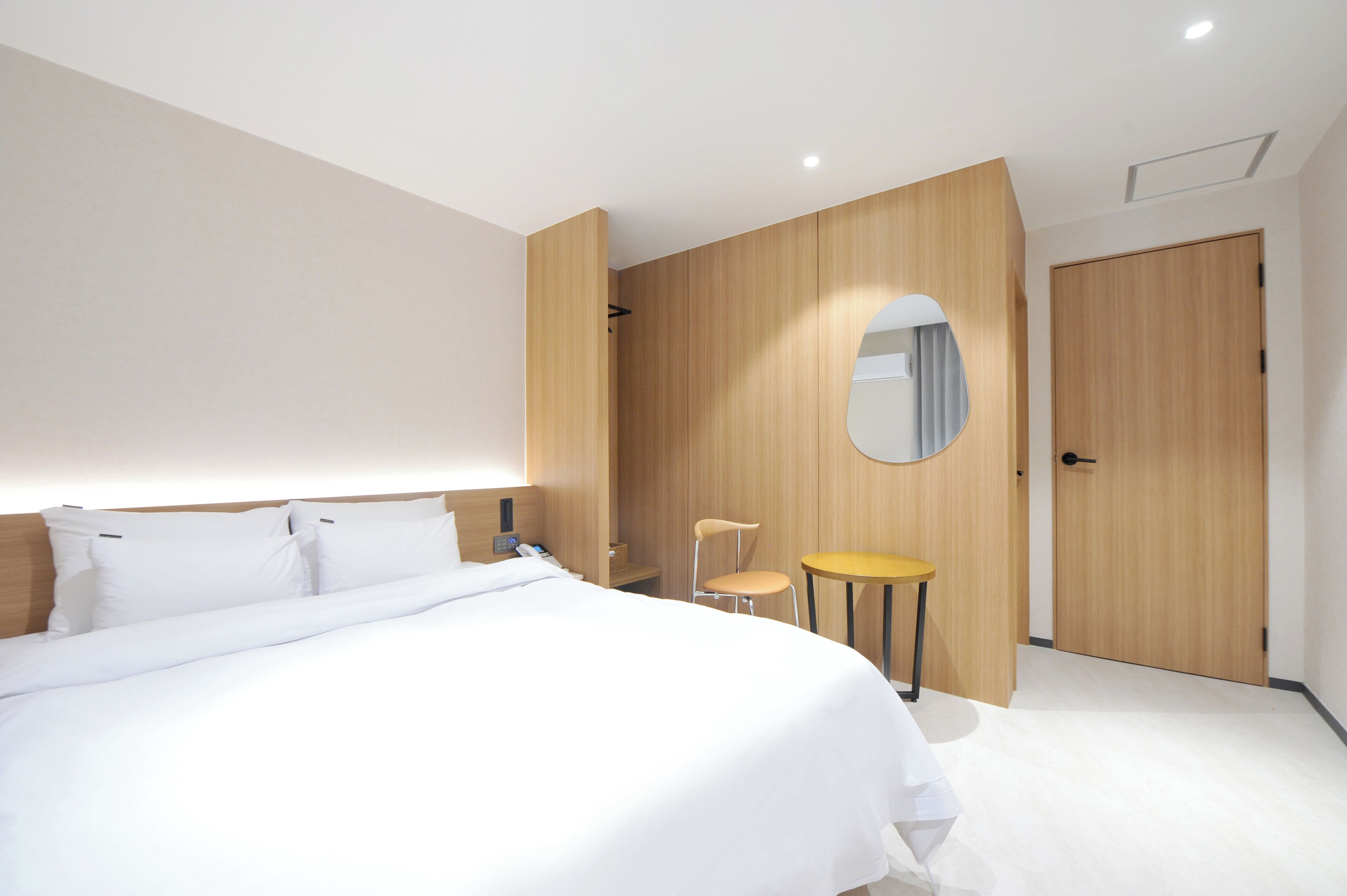 Quarto de hotel moderno com uma cama grande, uma mesa pequena, uma cadeira e um guarda-roupa de madeira.