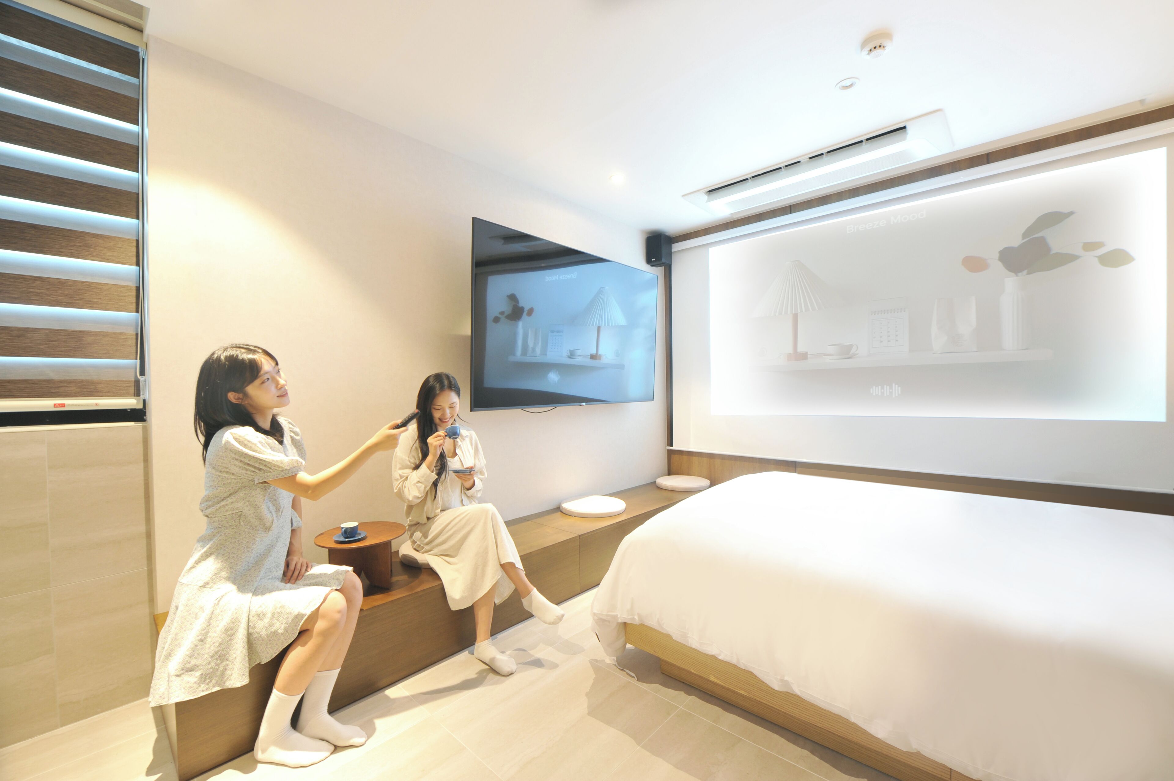 Una habitación de hotel moderna con una cama grande, un televisor de pantalla plana montado en la pared y un pequeño rincón de descanso con una mesa y sillas.