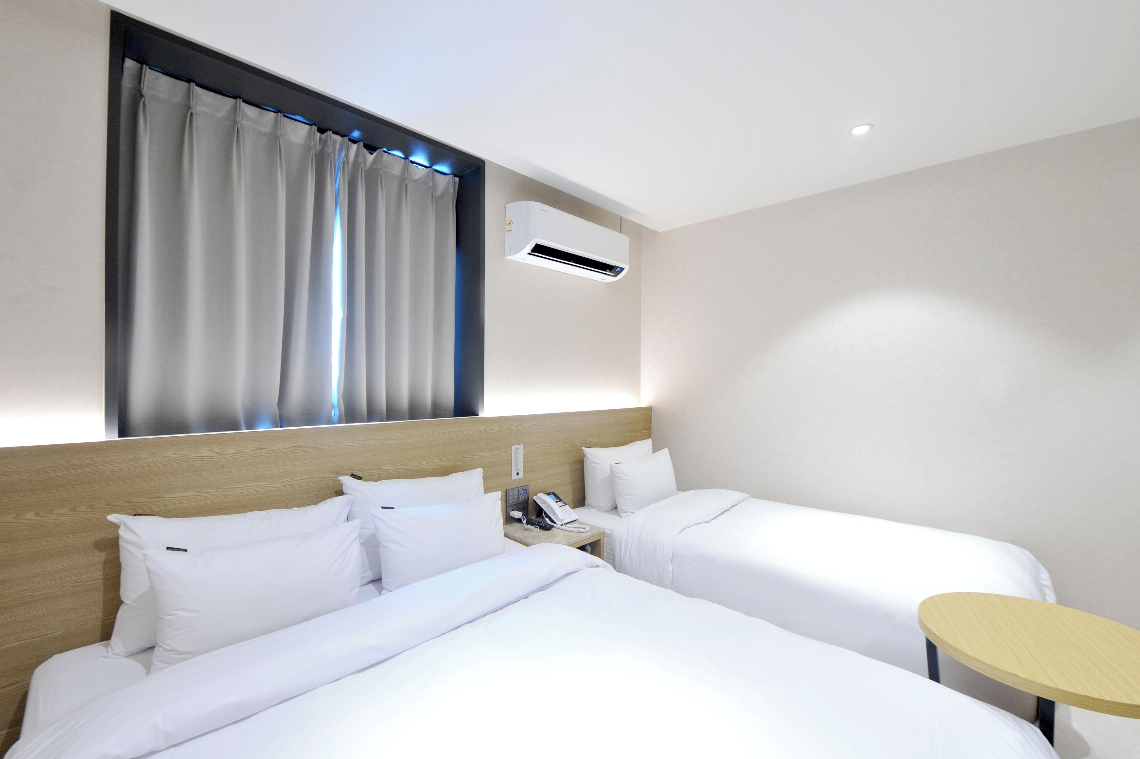 Ein Hotelzimmer mit zwei Betten, einem Holzkopfteil, einem Nachttisch mit Telefon und einem kleinen runden Tisch.