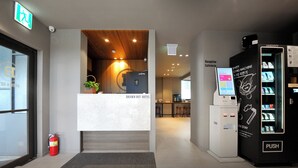 Zona de recepción de un hotel con mostrador de recepción, extintor, máquina expendedora y cartel de recepción.