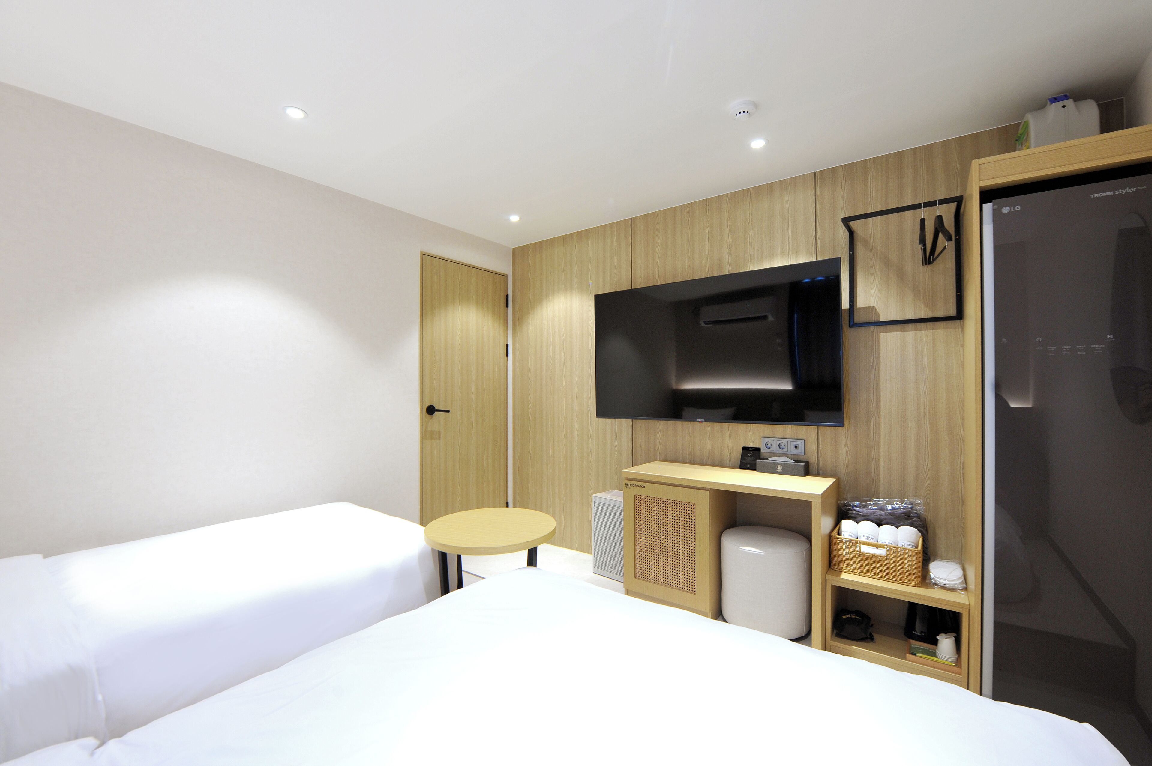 Una habitación de hotel moderna con dos camas individuales, una mesita redonda pequeña, un televisor montado en la pared y un minibar.
