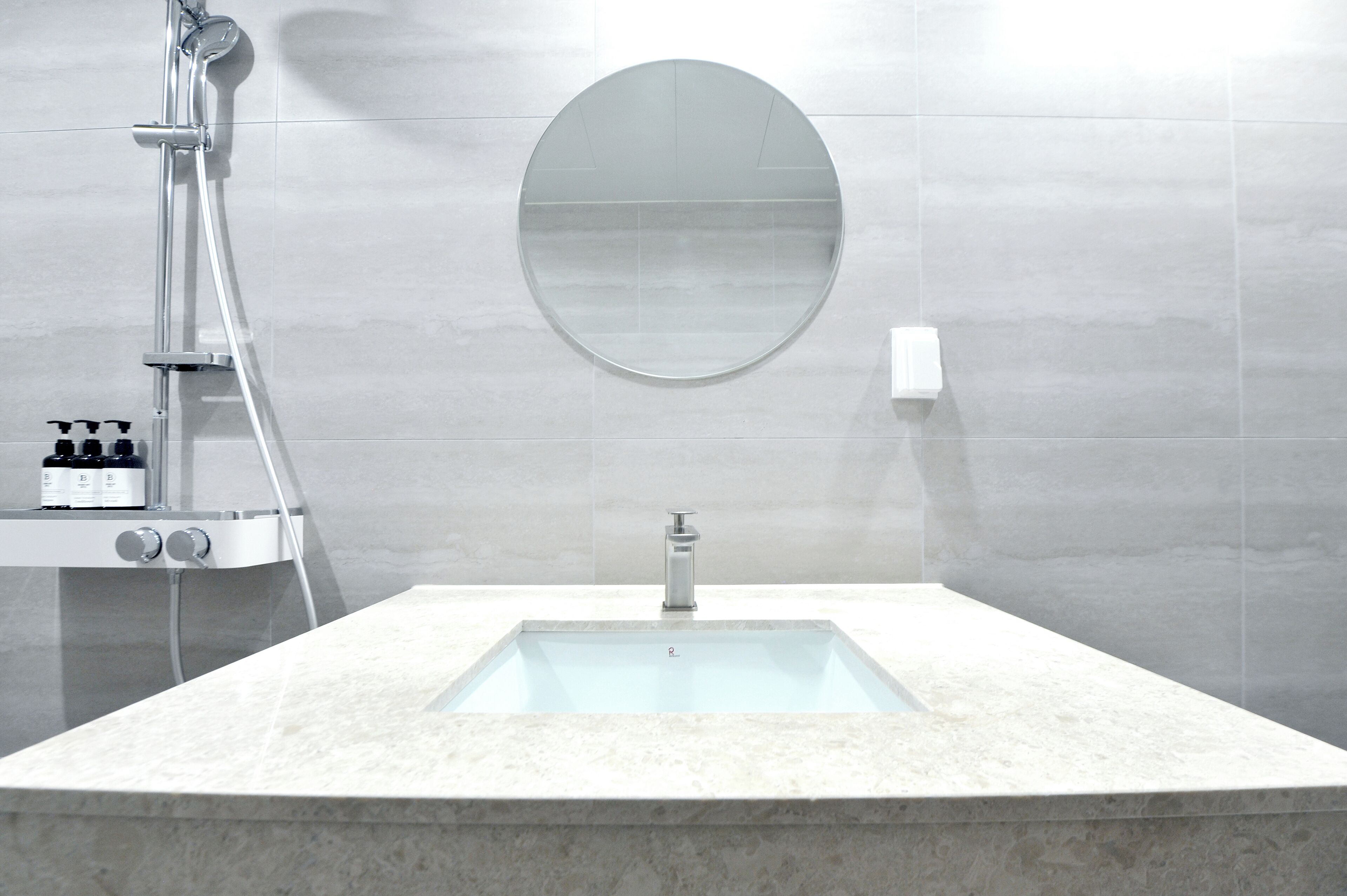Un baño moderno con un lavabo rectangular, un espejo redondo y un cabezal de ducha de mano.