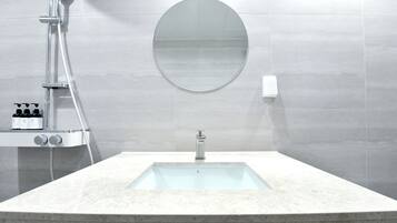 Un baño moderno con un lavabo rectangular, un espejo redondo y un cabezal de ducha de mano.