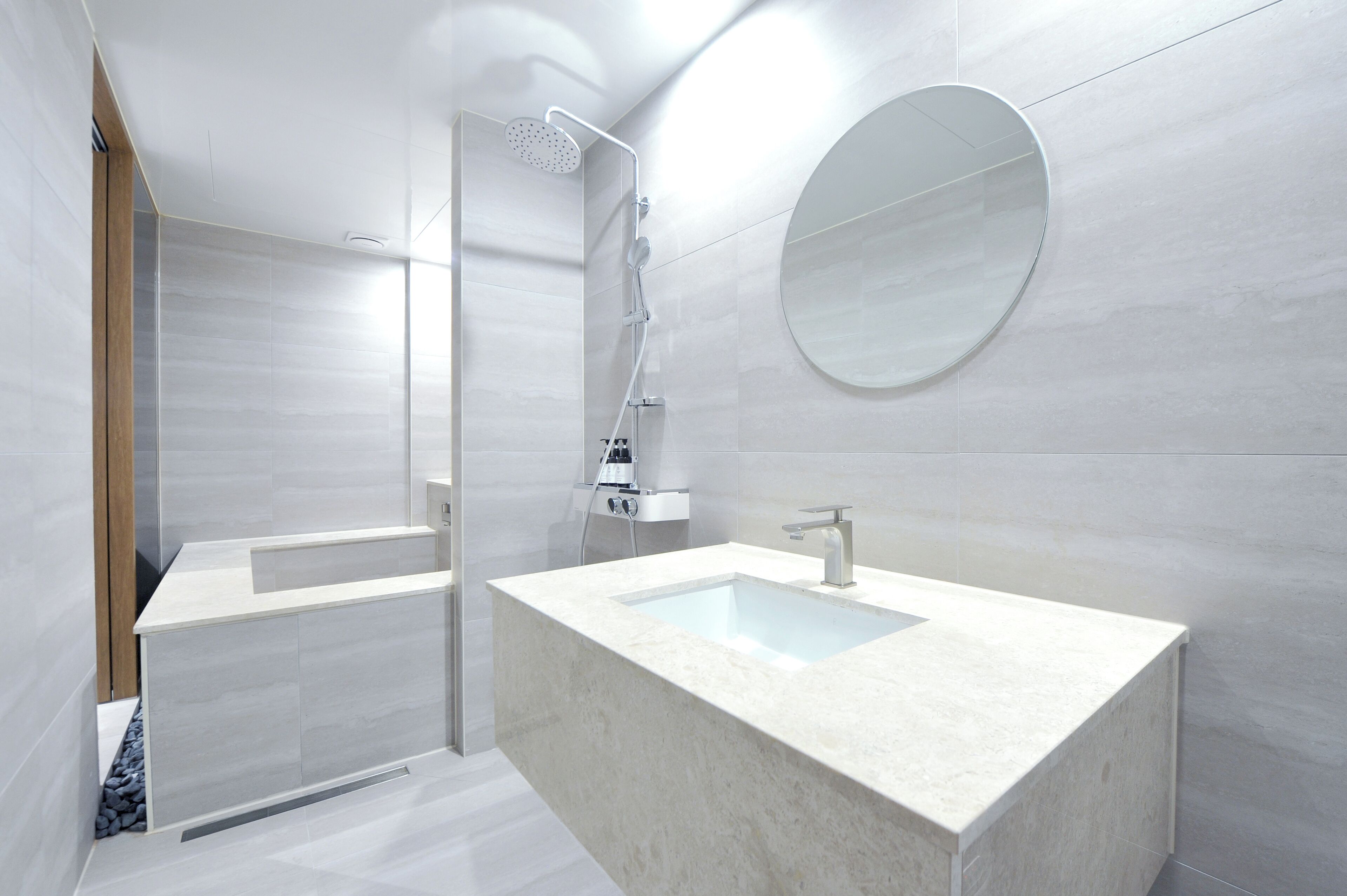 Un baño moderno con un lavamanos rectangular grande, un espejo redondo y una zona de ducha con mampara de cristal.
