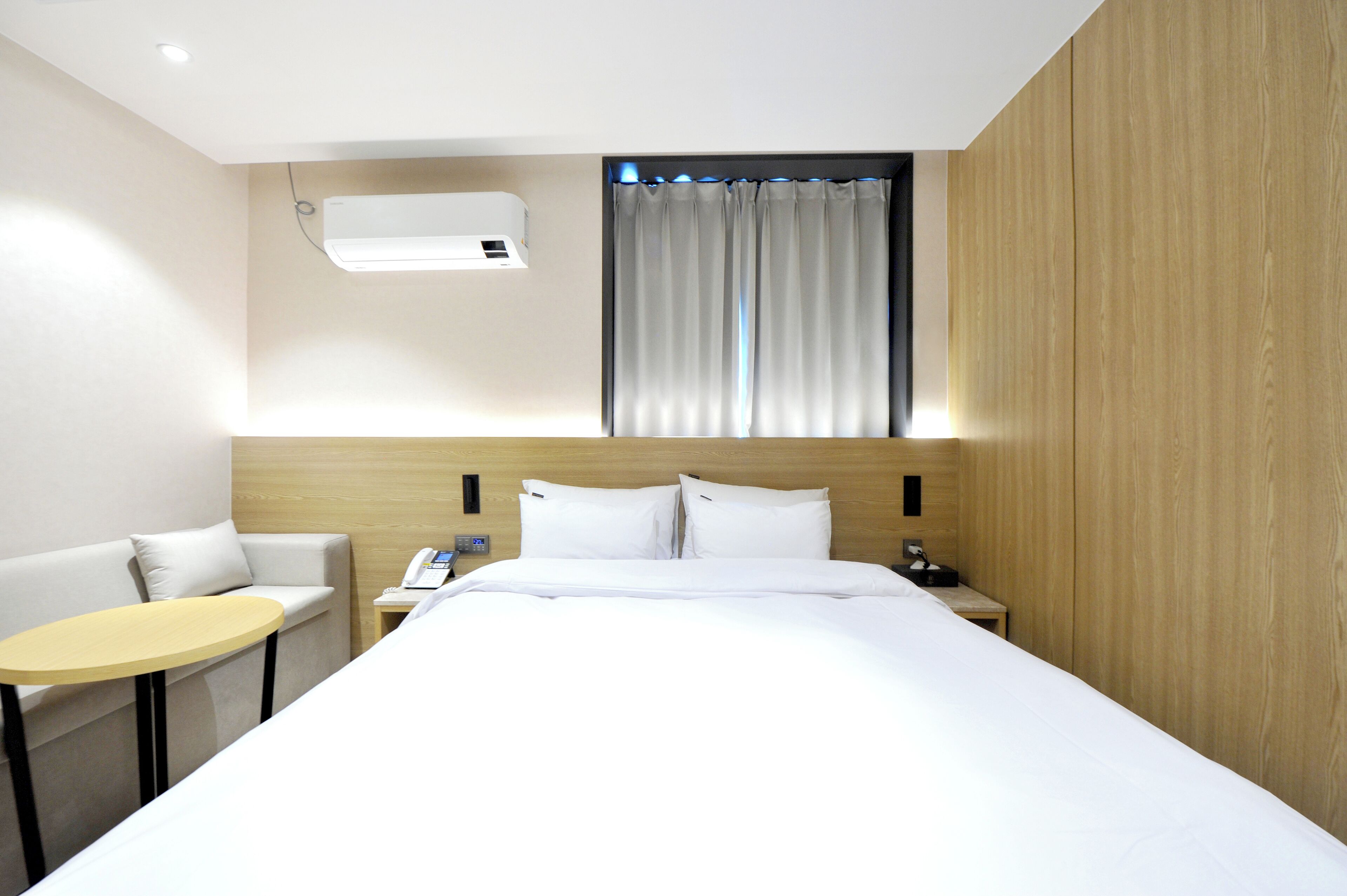 A hotel room with a bed, a small table, a sofa, a nightstand, and a window with curtains.