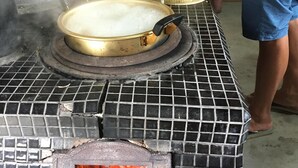 A kitchen with a tiled stove top, a pot on the stove, and a person cooking. - Stay, Experience, Discover!! Guest House Ilonggo -Filipino-Japanese Farm House- (Tsu)