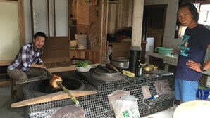 A kitchen with a large stove, a person cooking, and various kitchen items. - Stay, Experience, Discover!! Guest House Ilonggo -Filipino-Japanese Farm House- (Tsu)