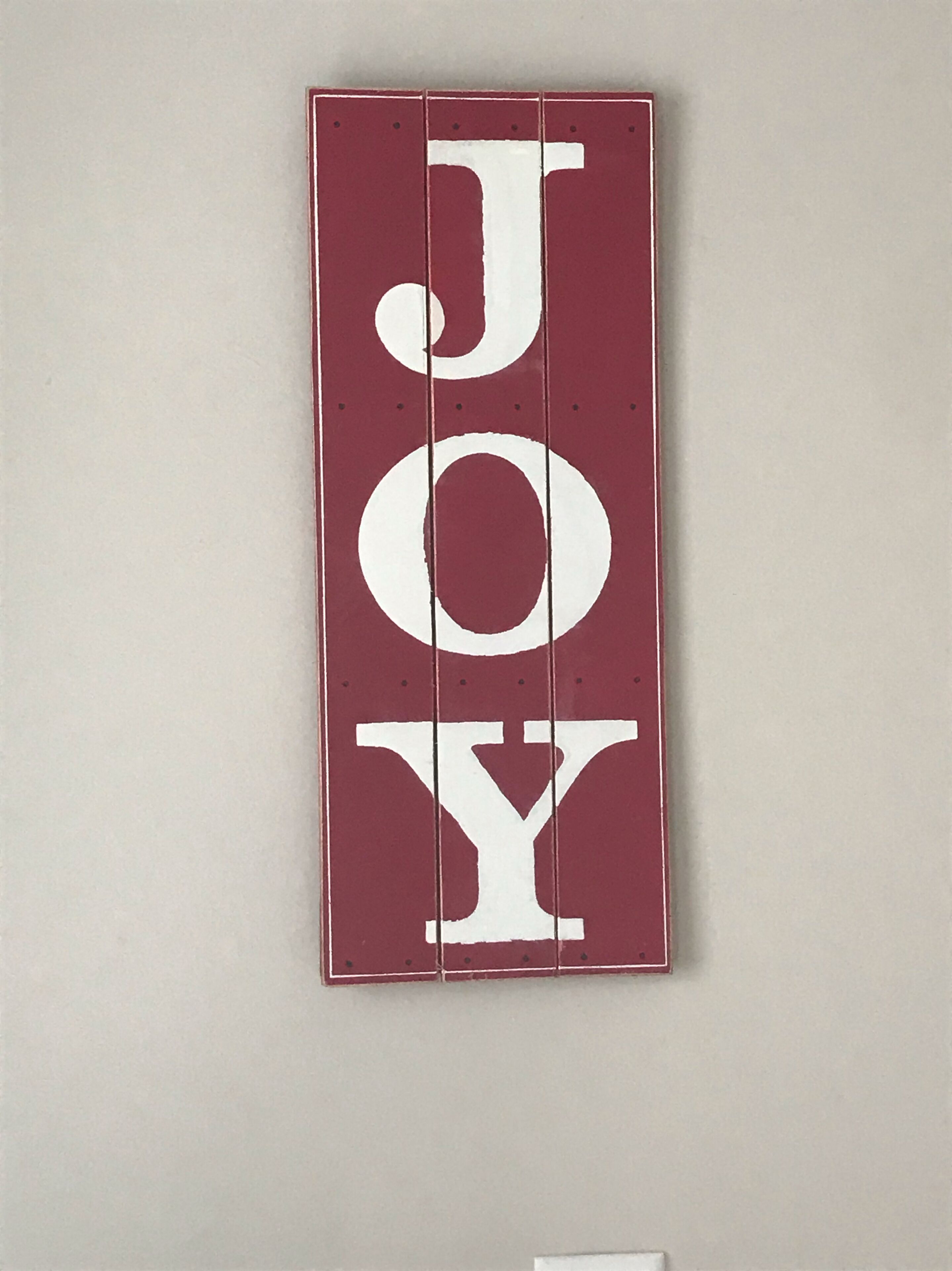A vertical sign with the word "JOY" in large white letters on a maroon background.