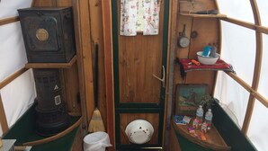 A rustic wooden interior with a vintage stove, a broom, and a small shelf with toiletries.