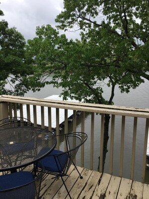 A wooden deck with a metal table and chairs, overlooking a calm body of water and a dock. - Recently Updated Waterfront Condo (Osage Beach)