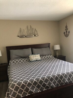 A bedroom with a bed, pillows, a nightstand, a lamp, and wall decorations including a ship and an anchor. - Recently Updated Waterfront Condo (Osage Beach)