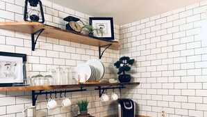 A kitchen with wooden countertops, white tiled backsplash, and shelves holding dishes, jars, and a coffee machine.