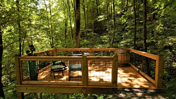 A wooden deck with a bench and a table, surrounded by a forest.