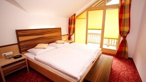 Un lit bien fait, avec une tête de lit en bois, une table de chevet avec une lampe et une vue sur un balcon agrémenté de rideaux.