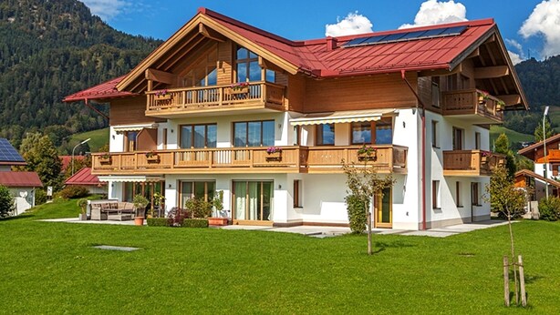 Une maison en bois à deux étages, dotée de balcons, d’un toit rouge et d’une pelouse verte.