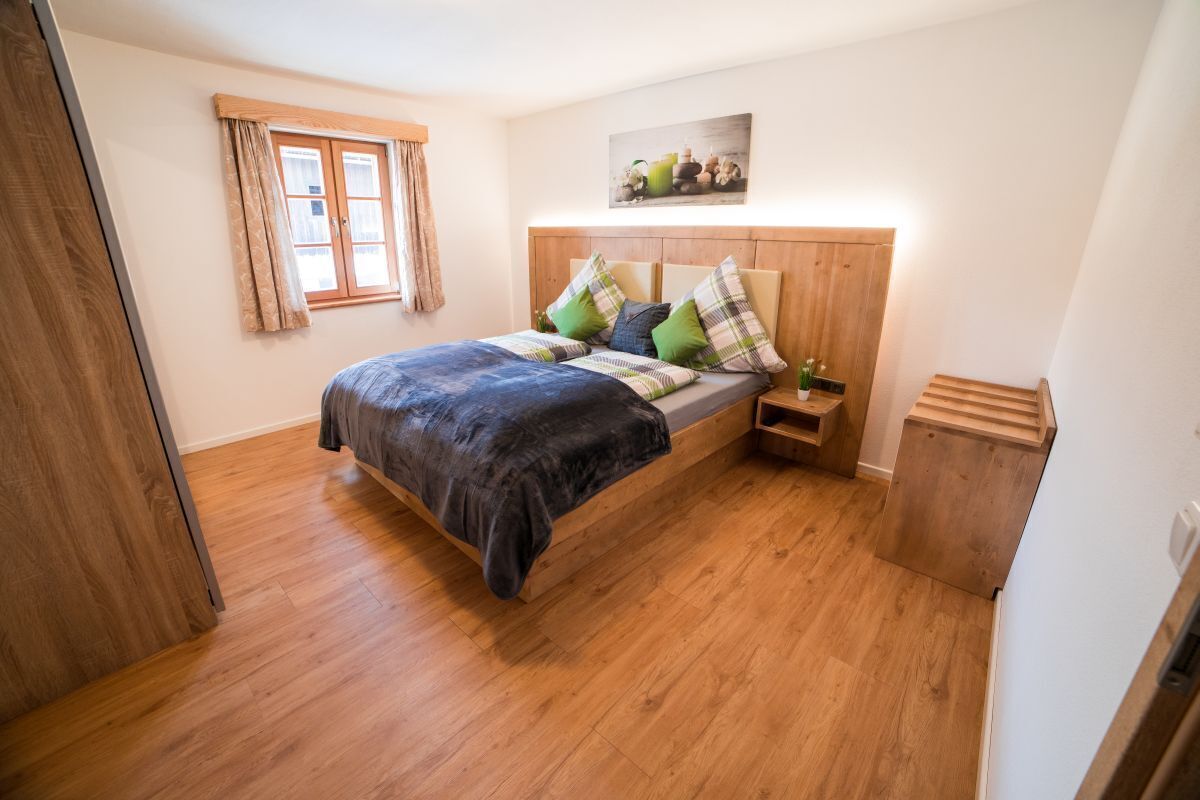 Un dormitorio con una cama de madera, una mesita de noche, un pequeño armario de madera y una ventana con cortinas.