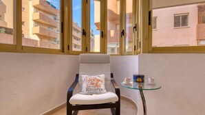 A balcony with a chair, a small table, and a view of neighboring buildings.