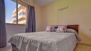 A bedroom with a bed, curtains, a window, and a wall-mounted shelf.