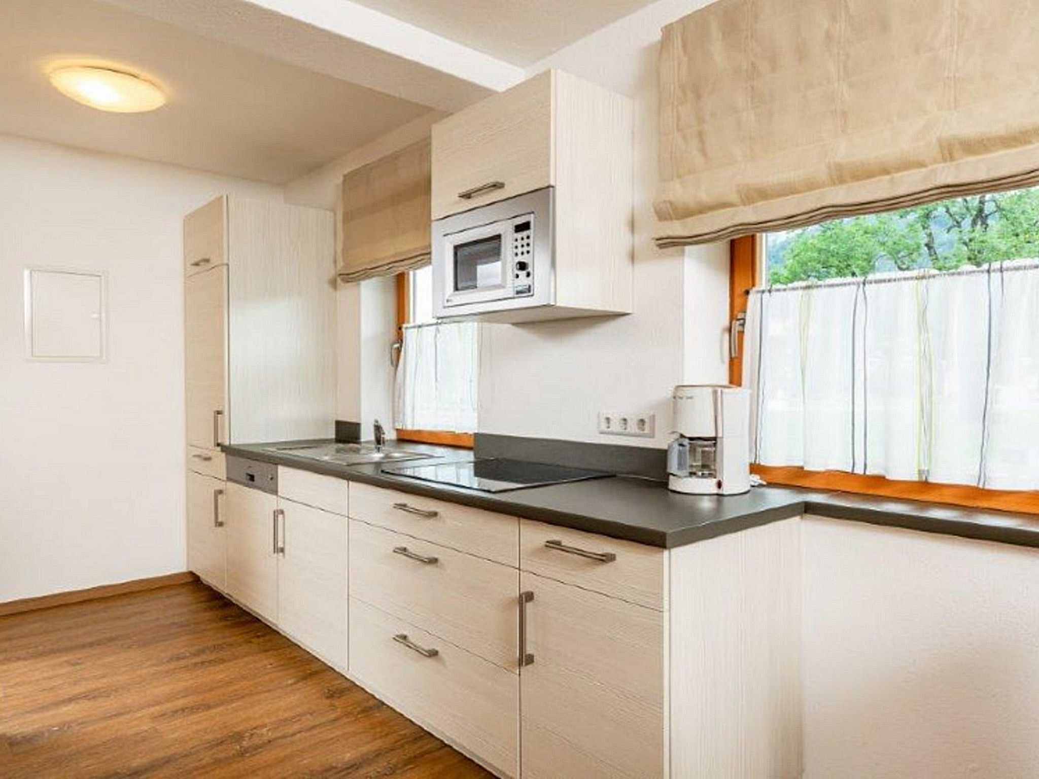 A compact kitchen with a microwave, coffee maker, and a window with curtains.