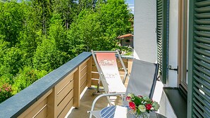 Ein Balkon mit Stuhl und Tisch, einem Holzzaun und Blick auf Bäume und ein Haus.