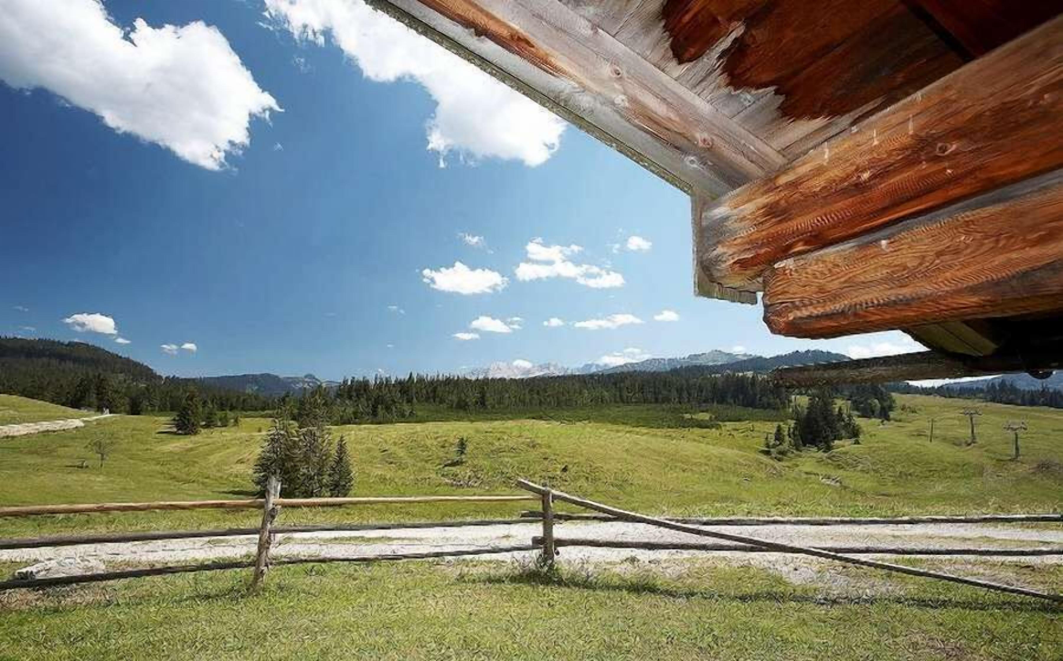 Una cabaña de madera con vistas a un valle verde y montañas lejanas.
