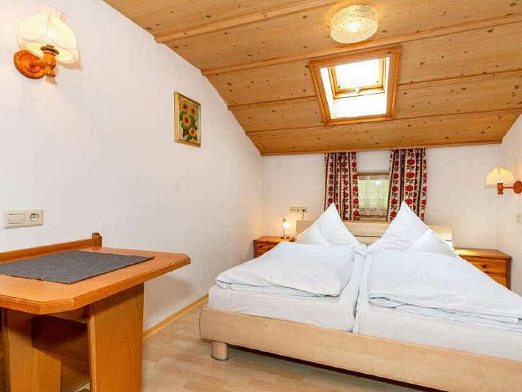 A cozy room with a bed, a desk, a window with curtains, and a ceiling light.