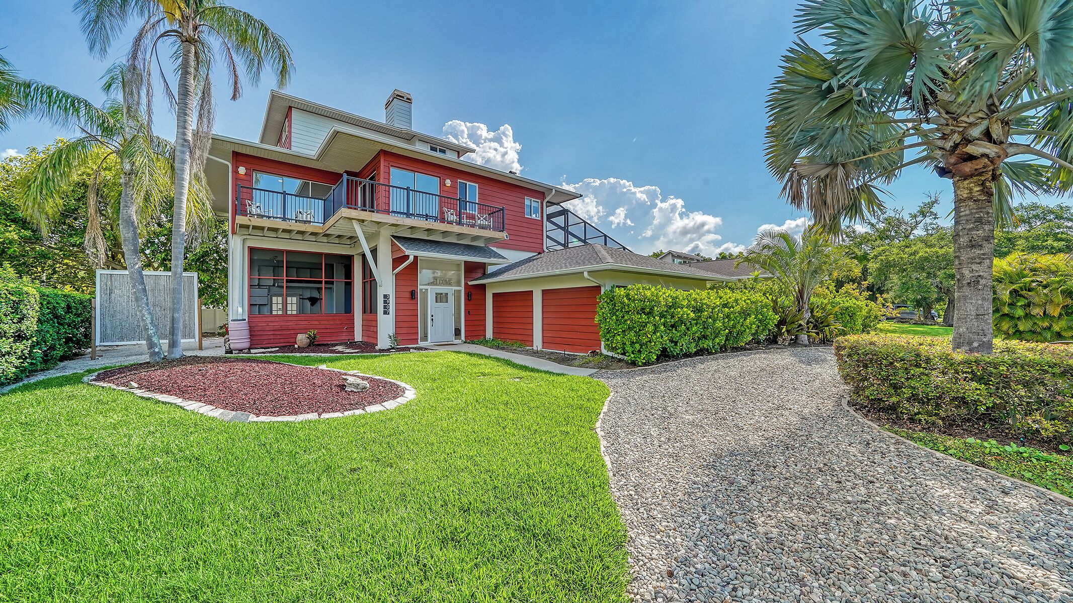 A two-story house with a red exterior, a covered front porch, and a driveway leading to the garage.