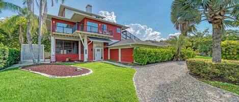 A two-story house with a red exterior, a covered front porch, and a driveway leading to the garage.