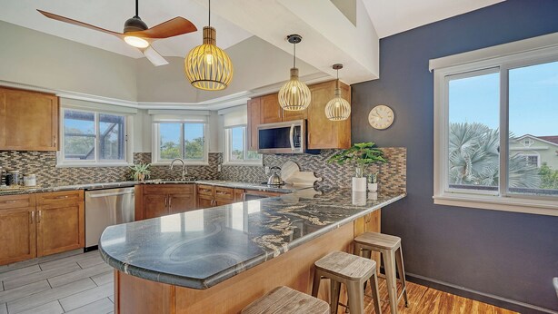 A modern kitchen with a large island, wooden cabinets, and pendant lighting. - Ocean View of AMI | Hot Tub | IMG | 6 TVs | 2 King Beds (Bradenton)
