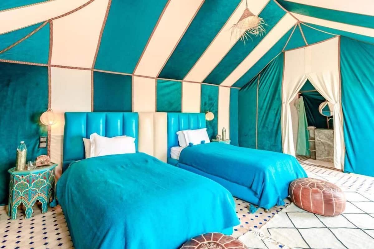 A room with two beds, a patterned floor, and a tent-like structure with teal and white colors.