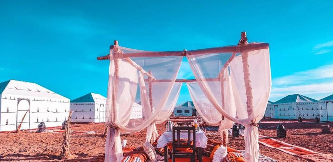 A traditional tent with a canopy, a dining table, and a chair in a desert setting with yurts in the background.