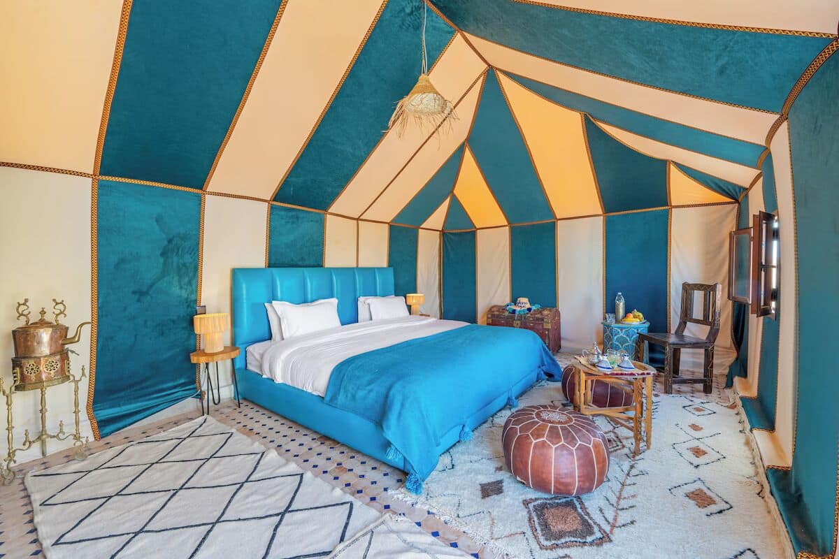 A tent-style bedroom with a bed, pillows, a lamp, a chest of drawers, a chair, and a patterned rug.