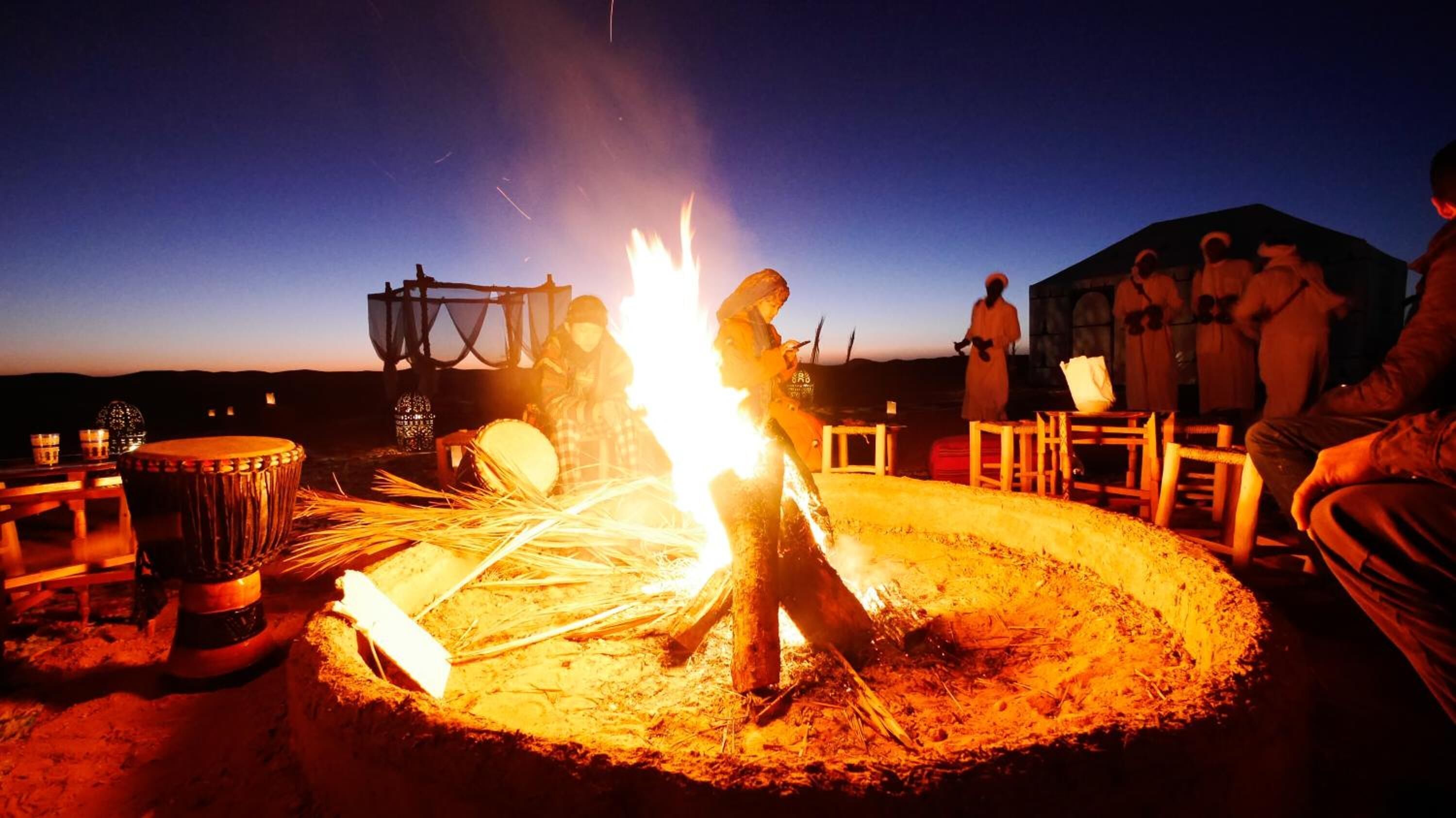 A campfire with people around it, a drum, and a lantern.