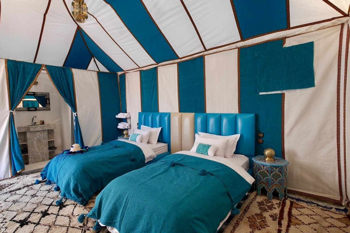 A tent-style room with two beds, a small bathroom, and a decorative nightstand.