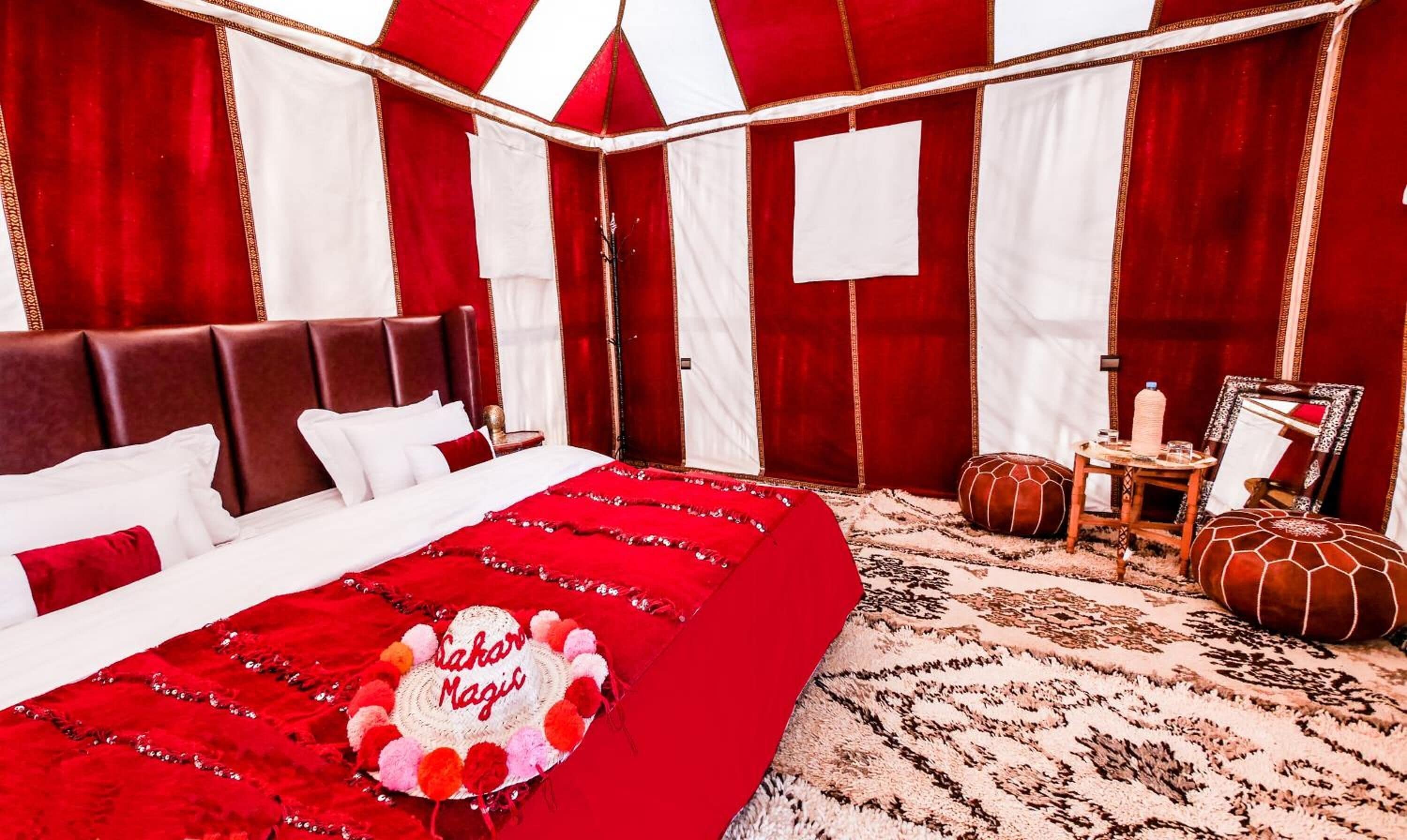 A room with a large bed, a small table, a mirror, and a patterned rug.