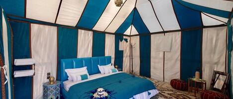 A tented room with a bed, a small table, and a chair.