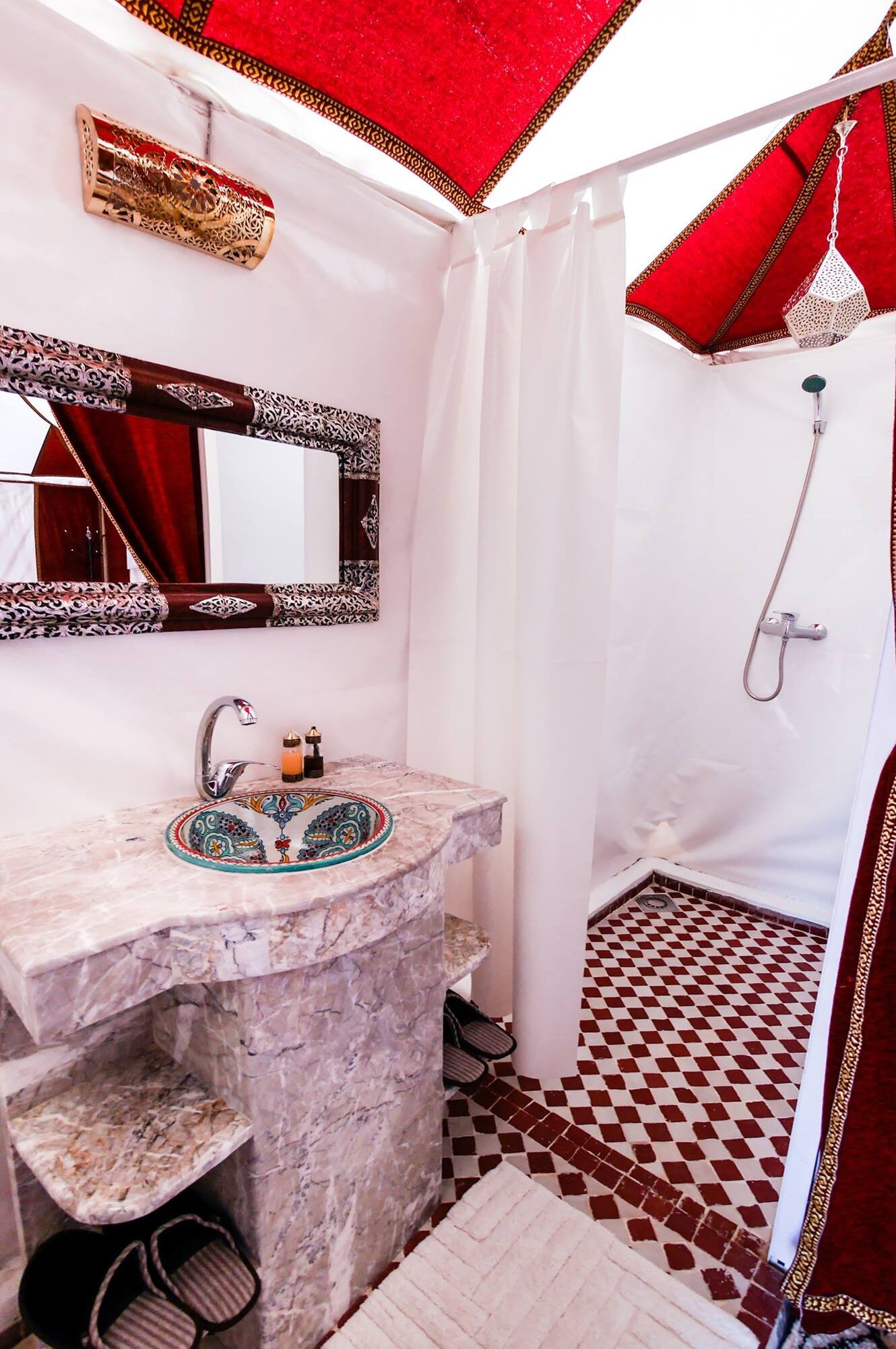 A bathroom with a marble sink, a mirror, a shower with a red curtain, and a patterned floor.