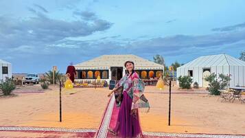 Paisaje desértico con una estructura tipo tienda, una persona con vestimenta tradicional y un vehículo.