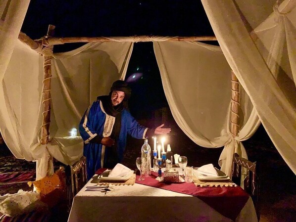 Una carpa con una mesa preparada para dos personas, velas y una botella de vino.