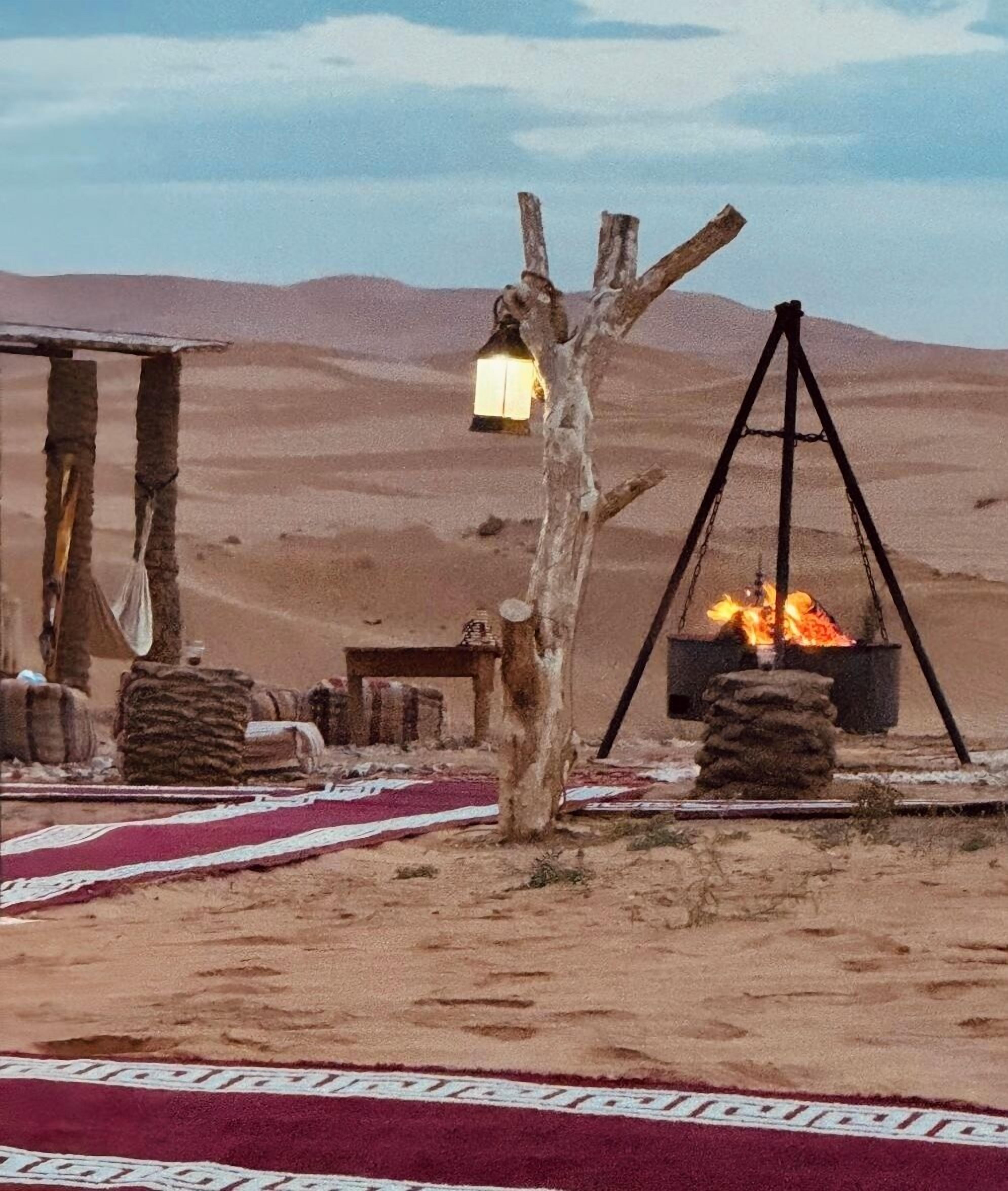 A desert scene with a traditional campfire setup, including a hanging lantern and a swing seat.