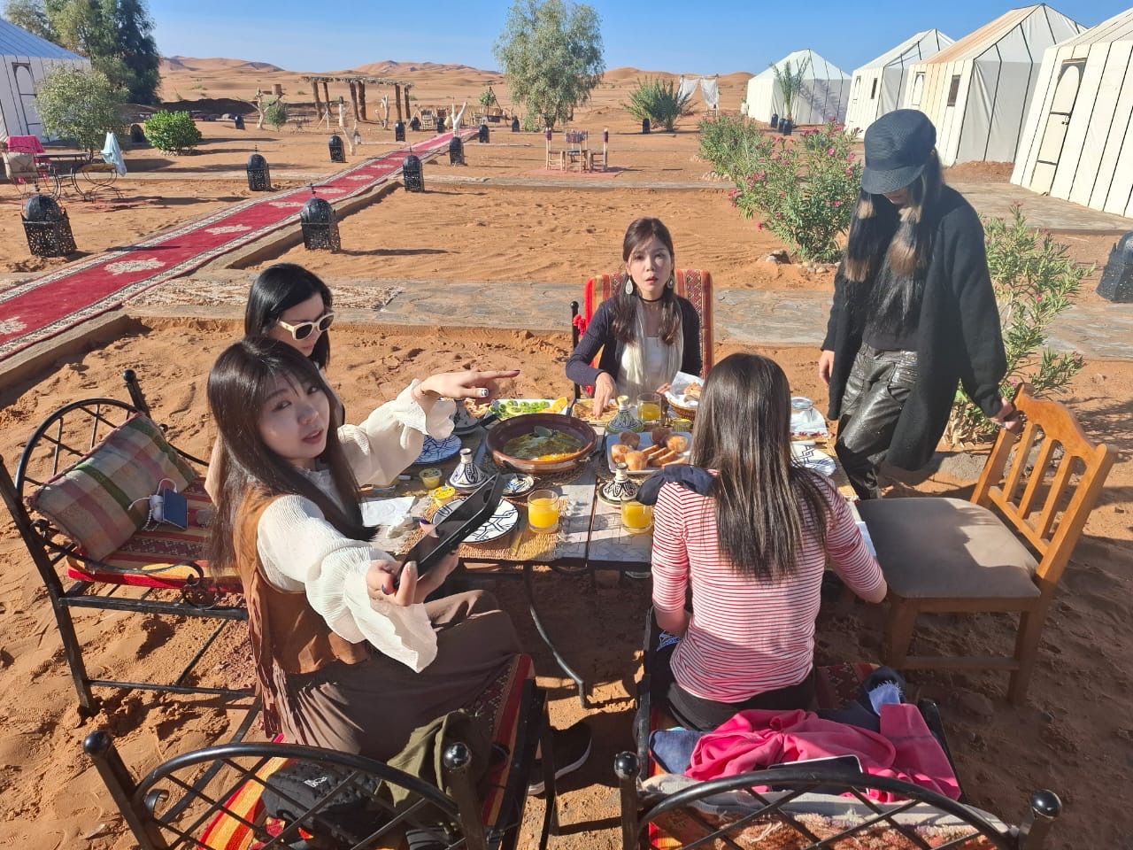 Een groep mensen dineert buiten met een woestijnlandschap op de achtergrond.