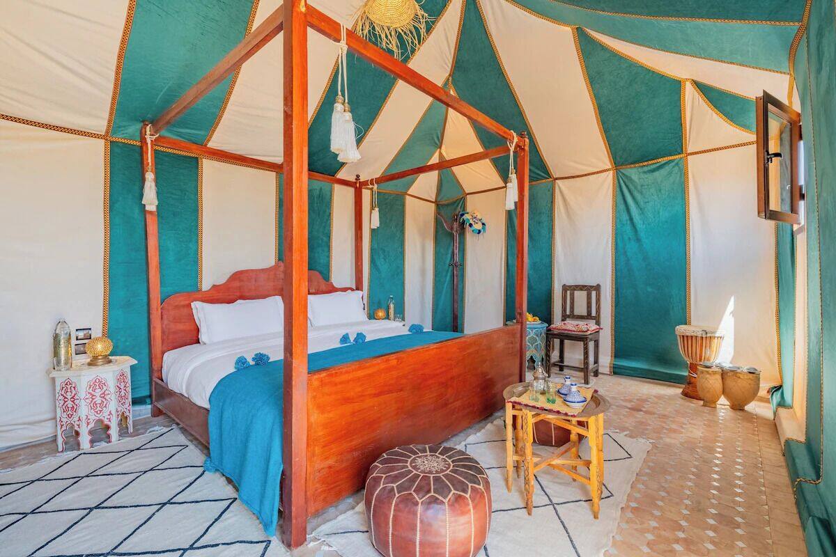 A four-poster bed in a tent-style room with a small table and ottoman.