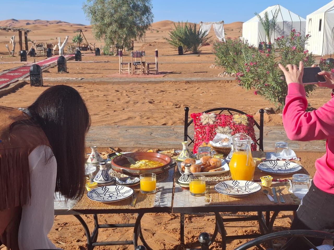 Un espace de restauration en plein air avec une table dressée pour le petit-déjeuner, entouré d’un paysage désertique et de tentes.