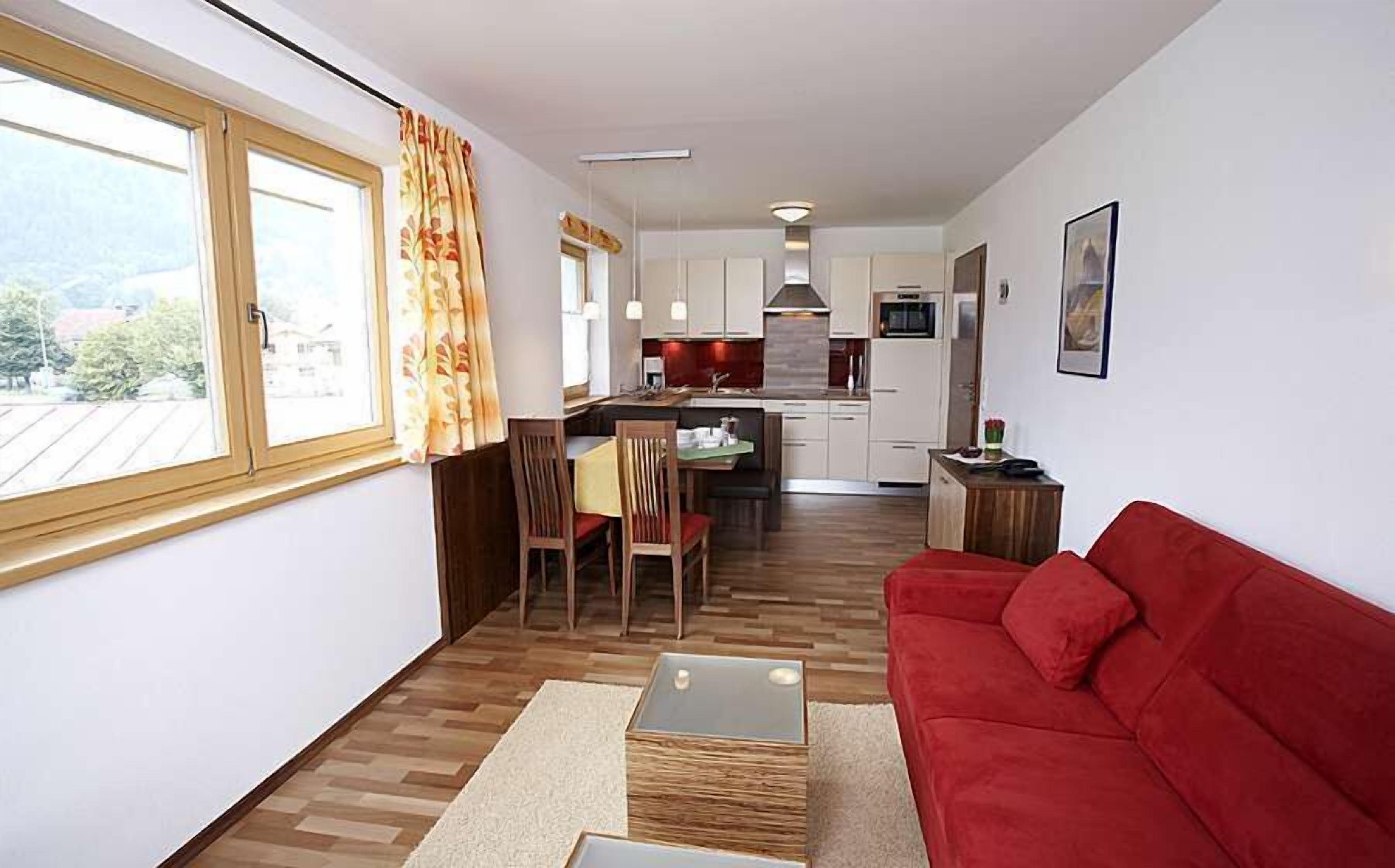 Un espace de vie compact comprenant un coin repas, une kitchenette et un canapé rouge.